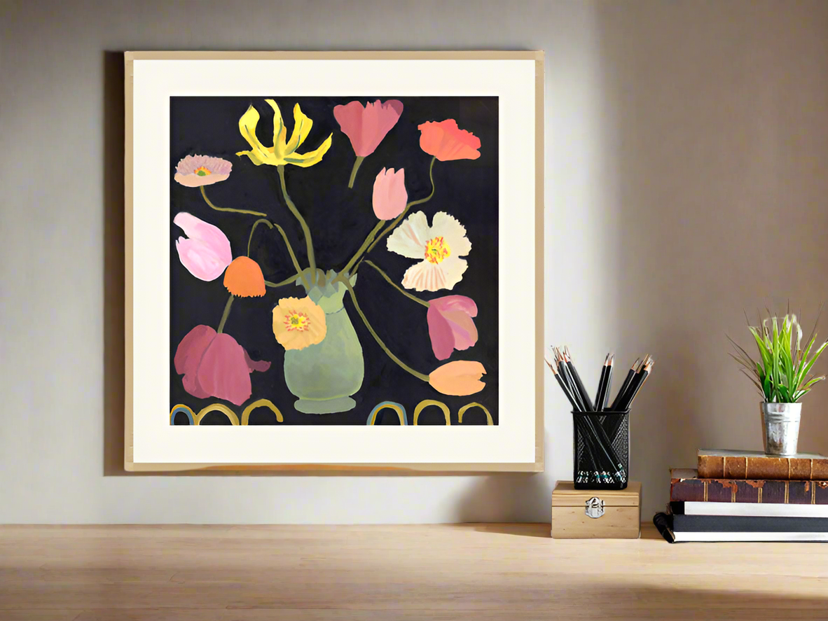 Framed Giclée flower print of tulips and poppies in a green vase, styled on a wooden desk with books and a small plant.