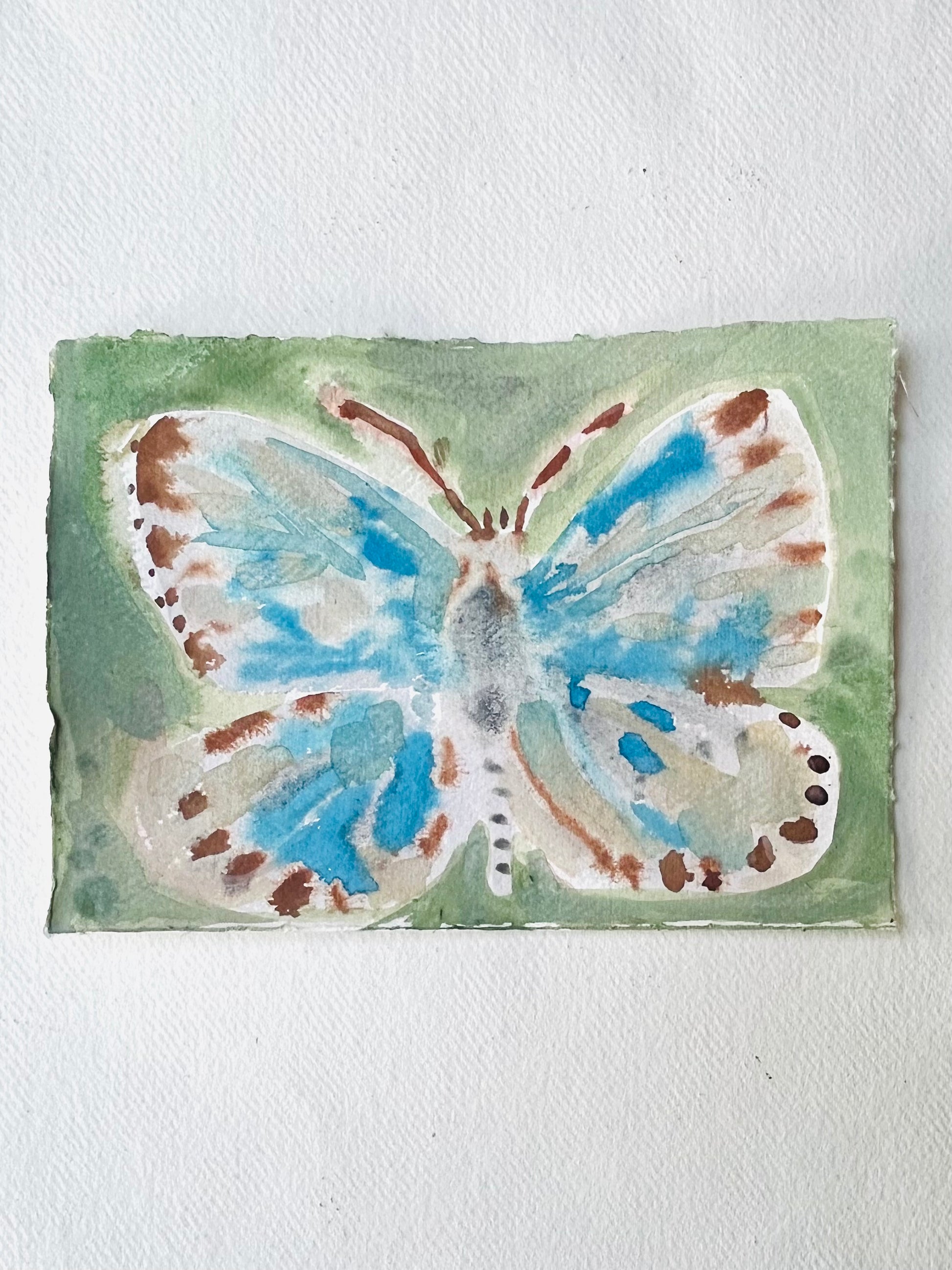 Butterfly No 7, a watercolor painting on paper featuring a blue and brown butterfly on a green background.