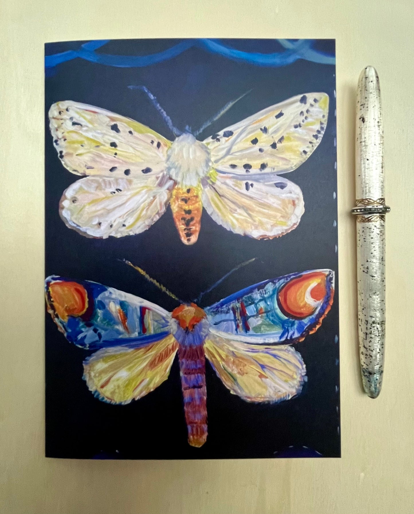 Fine art greetings cards featuring colorful butterfly illustrations on a dark background, with a silver pen beside them.